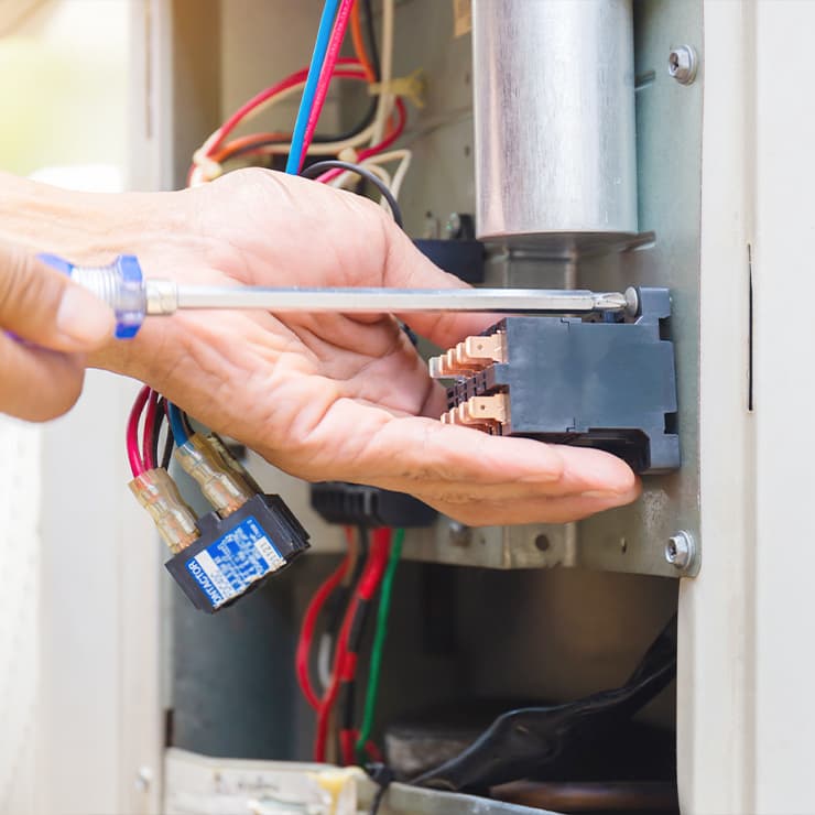 HVAC technician repairing electrical components inside an air conditioning unit.