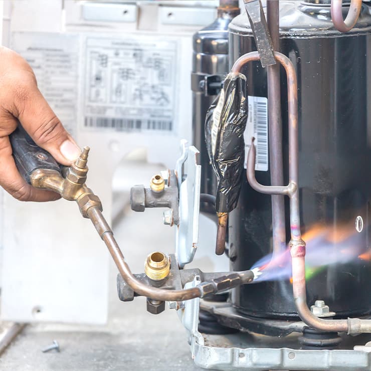 HVAC technician brazing copper refrigerant lines on an outdoor AC unit